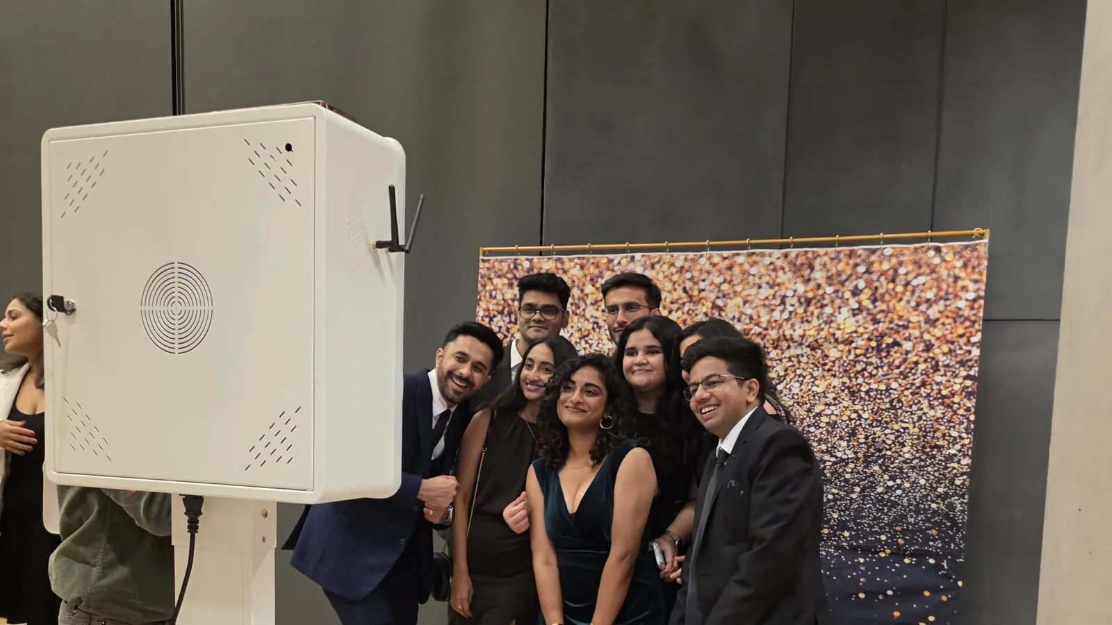 Students in formal wear posing at a photo booth in front of a sequin backdrop